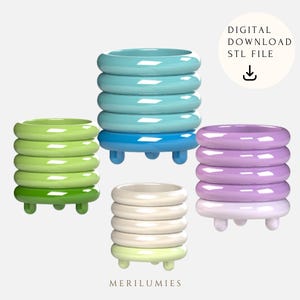 Puede incluir: Cuatro macetas impresas en 3D en diferentes colores: azul claro, verde, morado y blanco. Cada maceta tiene un diseño de anillos apilados y pequeños pies.