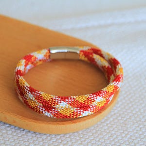 May include: A red, white, and yellow braided bracelet with a silver magnetic clasp.