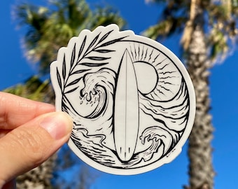 Puede incluir: Diseño de pegatina en blanco y negro de una tabla de surf con una ola y una hoja de palmera. La pegatina está sobre un fondo blanco.