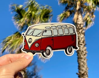 Puede incluir: Una pegatina de una furgoneta vintage roja y crema con un símbolo de la paz en la parte delantera. La furgoneta tiene neumáticos y ventanas blancas. La pegatina se sostiene contra un fondo de palmeras y un cielo azul brillante.