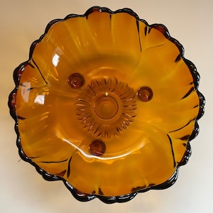 May include: A brown glass pedestal bowl with a scalloped edge and three feet. The bowl has a sunflower design in the centre.