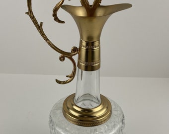 May include: A clear glass decanter with a gold-tone metal top and handle. The decanter has a diamond-shaped pattern on the body and a round base.