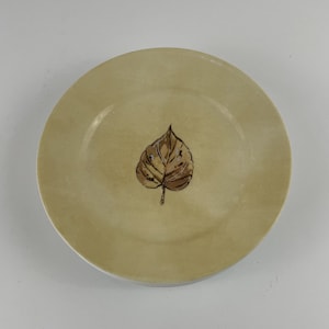 May include: A beige ceramic plate with a brown leaf design in the centre.