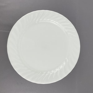 Peut inclure: Une assiette à dîner blanche et ronde avec un motif de volutes en relief subtil sur le bord. L'assiette a une finition lisse et brillante et convient pour servir les repas. Design classique.