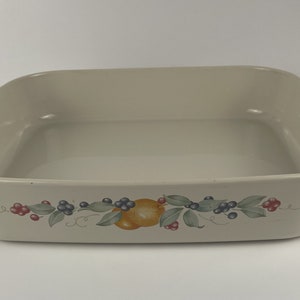 May include: A white ceramic baking dish with a floral design featuring fruit and berries. The dish has a square shape with rounded corners and a slightly raised rim.