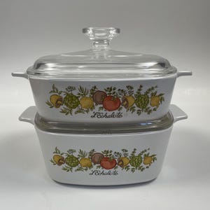 May include: A white ceramic casserole dish with a glass lid. The dish features a floral design with vegetables and the text "L'Echalote".