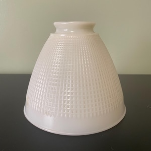 May include: A conical, off-white glass lampshade featuring a textured grid pattern of small, raised squares across its exterior surface. The shade has a smooth, circular opening at the top and a wider, flared base with a clean, finished edge.