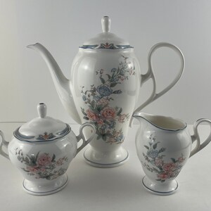 Puede incluir: Un juego de té de porcelana blanca con un patrón floral. El juego incluye una tetera, una jarra de crema y un azucarero.