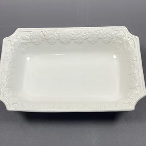May include: A white rectangular serving dish with a floral design around the edge. The dish has a smooth, glossy finish, suitable for serving starters or puddings. The dish is made of ceramic.