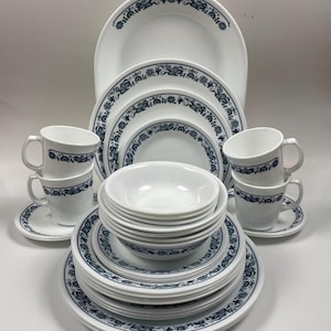 Puede incluir: Un juego de vajilla Corelle blanca con un patrón floral azul. El juego incluye platos, tazones y tazas.