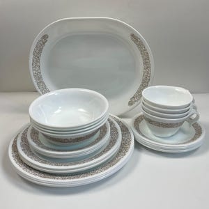 Puede incluir: Un juego de vajilla blanco con un diseño floral marrón. El juego incluye una fuente ovalada, cuencos, platos y tazas de té con platillos. Los artículos están apilados ordenadamente, mostrando un juego de comedor completo.