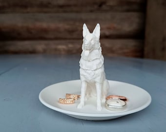 May include: White ceramic dog figurine ring holder with three gold rings on a white ceramic dish.