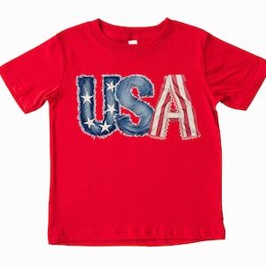 A red t-shirt with the word "USA" printed on it, featuring the letters in a stylized, distressed font.