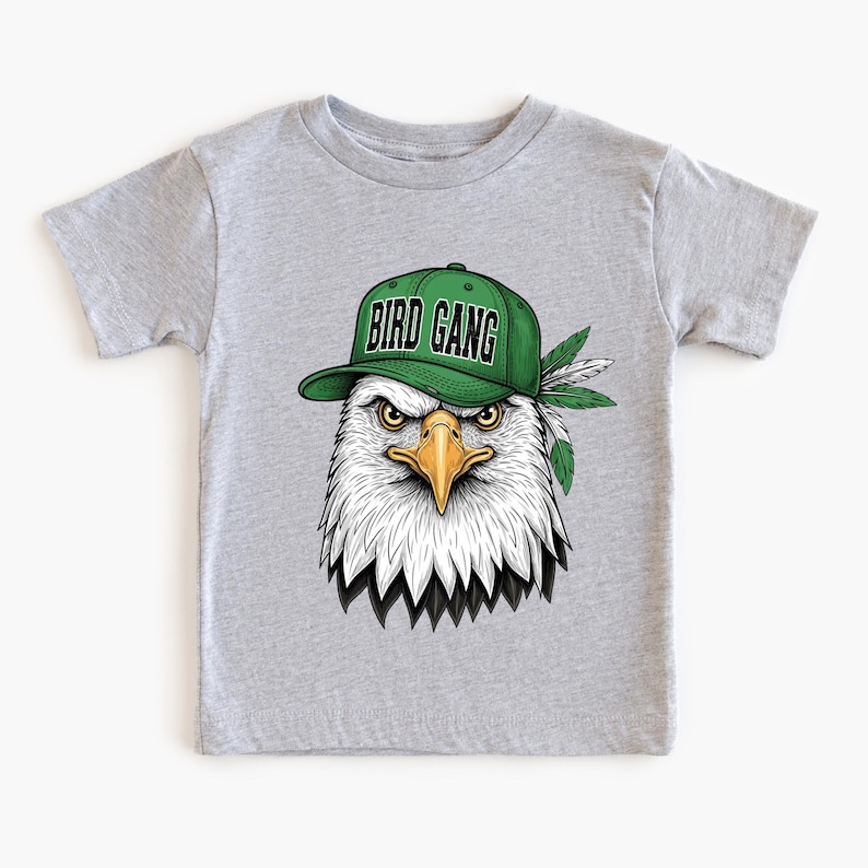 A gray t-shirt with a graphic design of an eagle wearing a green baseball cap with the text "BIRD GANG" printed on it.