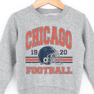 A grey sweatshirt with a graphic design featuring a football helmet and the text "CHICAGO FOOTBALL" printed on it.