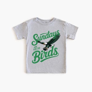 A grey t-shirt with a graphic design featuring a green eagle and the text "SUNDAYS ARE FOR THE BIRDS" printed on it.