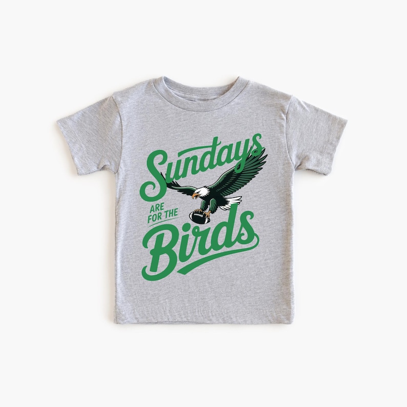 A grey t-shirt with a graphic design featuring a green eagle and the text "SUNDAYS ARE FOR THE BIRDS" printed on it.