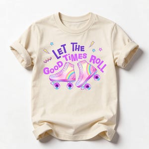 A beige t-shirt with a graphic design featuring roller skates and the text "Let the good times roll" in a colorful, playful style.
