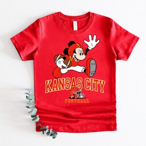 A red t-shirt with a cartoon image of Mickey Mouse holding a football and the text "KANSAS CITY FOOTBALL" printed on it.