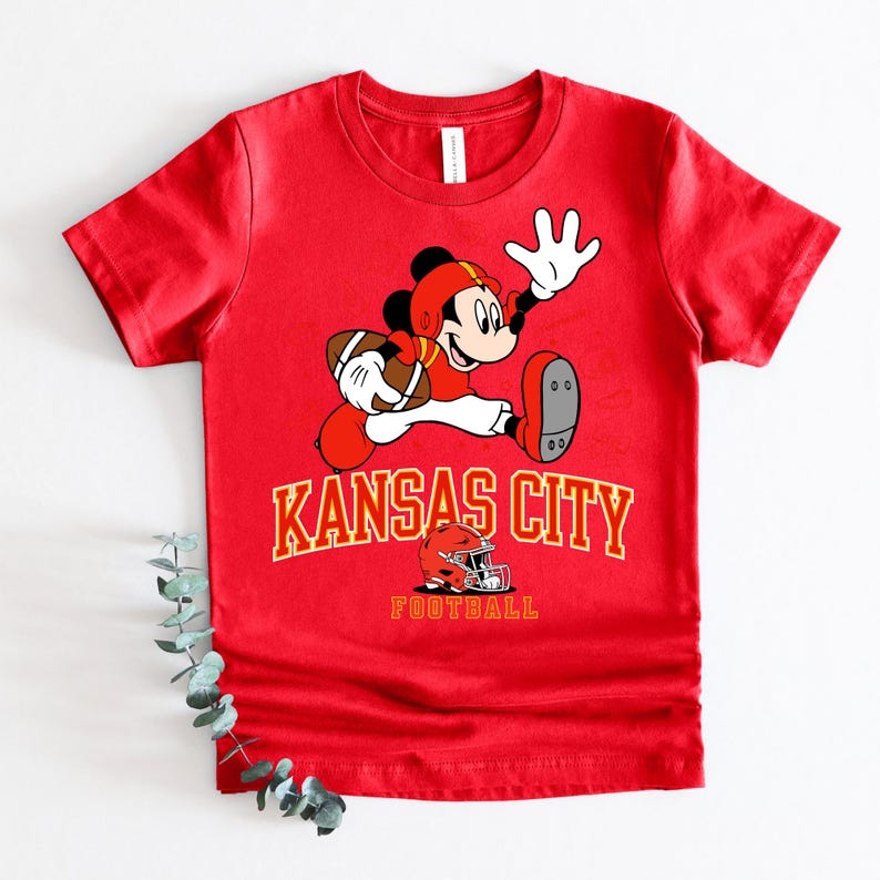 A red t-shirt with a cartoon image of Mickey Mouse holding a football and the text "KANSAS CITY FOOTBALL" printed on it.