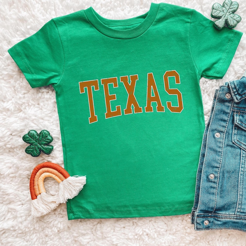 a green shirt with the word texas on it next to a pair of jeans and