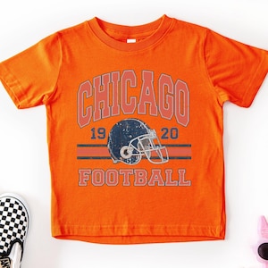 An orange t-shirt with a graphic design featuring a football helmet and the text "CHICAGO FOOTBALL" printed on it.