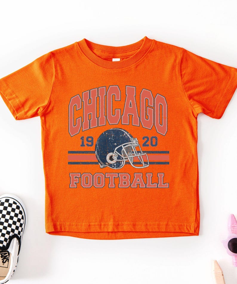 An orange t-shirt with a graphic design featuring a football helmet and the text "CHICAGO FOOTBALL" printed on it.