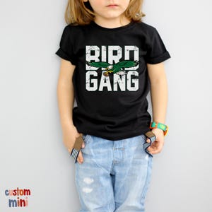 a little girl wearing a bird gang t - shirt