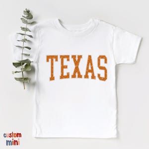 a t - shirt with the word texas on it next to a plant