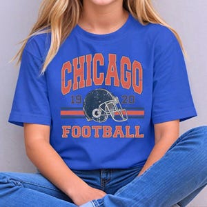 A young woman wearing a blue t-shirt with the text "CHICAGO FOOTBALL" and a graphic of a football helmet.