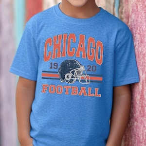 A young boy wearing a blue t-shirt with the text "CHICAGO FOOTBALL" and a graphic of a football helmet.