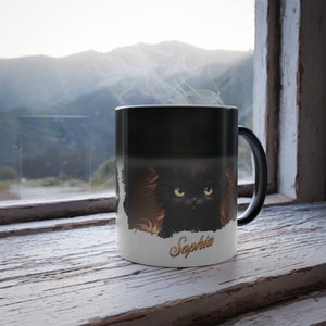 May include: Black magic mug featuring a black cat image that appears when hot liquid is added. The mug has the name "Sophia" written on the bottom in gold lettering.