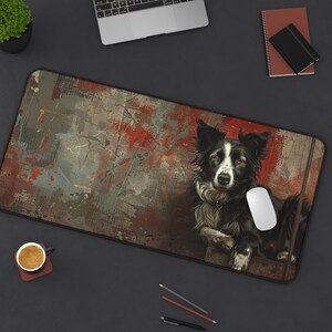 May include: A rectangular desk mat featuring a detailed illustration of a Border Collie dog. The dog is black and white with brown eyes, set against a textured background of red, gray, and brown paint strokes. A white computer mouse rests on the mat.