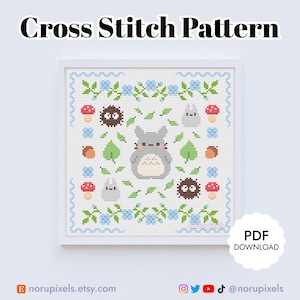 May include: Cross stitch pattern featuring a gray Totoro character surrounded by green leaves, blue flowers, red mushrooms, and brown acorns. The pattern is framed in a white frame with a blue and white border.