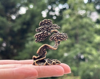 May include: A small, detailed bronze sculpture of a bonsai tree with a twisted trunk and branches. The tree is set on a rocky base.