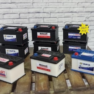 May include: Assortment of miniature car batteries in various brands, including Varta, Motorcraft, and Unipart. The batteries are stacked on a wooden pallet. A yellow sign reads "SALE! $4.75".