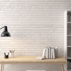 Könnte beinhalten: Eine weiße Backsteinwand mit einem Holztisch und einem weißen Bücherregal mit Büchern. Eine schwarze Lampe steht auf dem Tisch mit einem Stiftehalter und einem Buch.