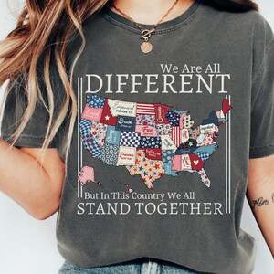 May include: Dark gray t-shirt with the text "We Are All DIFFERENT But In This Country We All STAND TOGETHER." The shirt features a colorful patchwork map of the United States.
