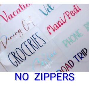 May include: A collection of clear adhesive labels featuring various text in different colors and fonts, including Vacation, Vet, Dining Out, Mani/Pedi, Groceries, Phone Bill, Coffee, and Road Trip. The text NO ZIPPERS is printed in blue at the bottom.