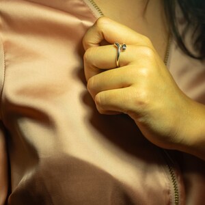 K&ouml;nnte beinhalten: Nahaufnahme einer Hand, die einen silbernen Ring mit einem einzigartigen Design tr&auml;gt. Der Ring befindet sich am Mittelfinger und besteht aus einem d&uuml;nnen, gebogenen Band mit einem kleinen, runden Detail oben.