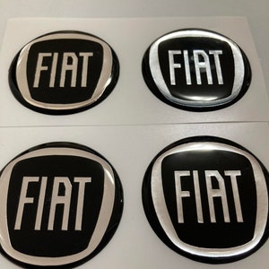 Könnte beinhalten: Vier schwarze und silberne 3D-Autoembleme mit dem Wort "FIAT" in weißen Buchstaben.