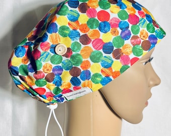 May include: A white scrub hat with a colorful polka dot pattern. The hat has a button on the top and a drawstring tie. The hat is made by RosesSewingRoom.