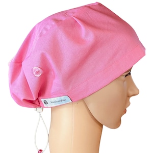 May include: A pink surgical scrub cap with a button and adjustable drawstring. The cap is made of a solid pink fabric and has a tag that reads "RosesSewingRoom". The cap is designed to be worn in a medical setting.