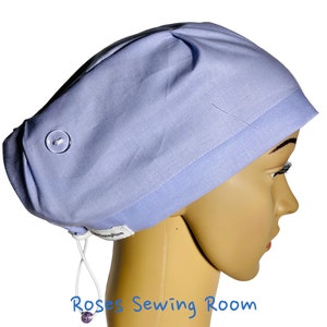 May include: A light blue scrub hat with a white button and a white drawstring. The hat is made of a soft, comfortable fabric and is ideal for healthcare professionals.