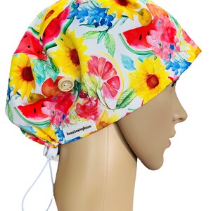 May include: A white scrub hat with a colourful floral print featuring watermelons, sunflowers, and citrus fruits. The hat has a white drawstring and a button on the top. The text "RosesSewingRoom" is printed on the hat.