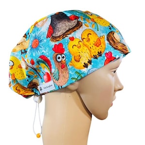 May include: A blue surgical scrub cap with a colorful chicken and chick pattern. The cap features a rooster, chicks, eggs, and flowers. It has a white drawstring for adjustment and a small tag with text.