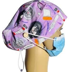 May include: Purple scrub hat with a tie and a button closure. The hat has a print of medical symbols, including a brain, a test tube, a pregnancy test, and a syringe. The hat is worn on a mannequin with a blue surgical mask.