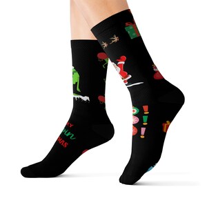 May include: Black Christmas socks with festive designs. One sock features a green character on a snowy hill, with the text "Merry Grin Christmas." The other sock has Santa Claus, reindeer, and gift boxes. A fun holiday accessory.