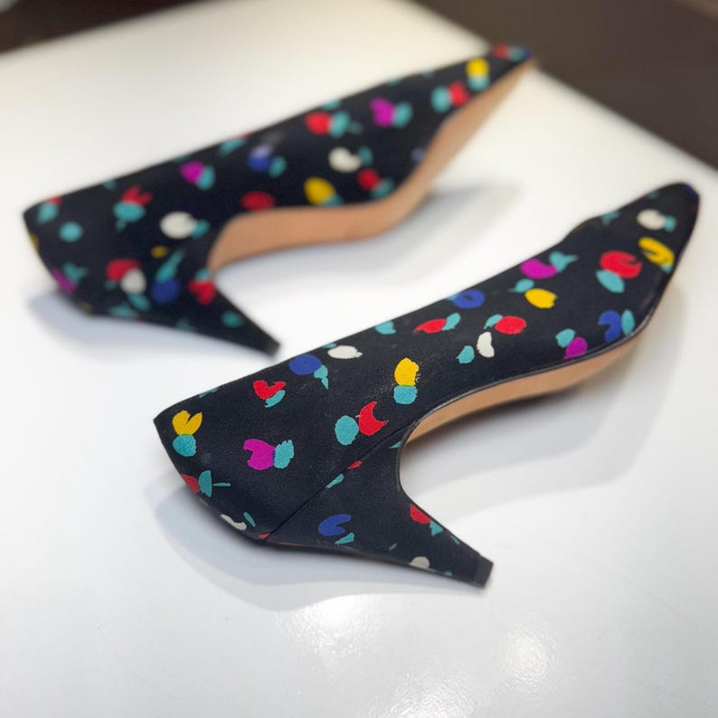 Puede incluir: Un par de zapatos de tac&oacute;n negros con punta y tac&oacute;n bajo. Los zapatos est&aacute;n cubiertos con un colorido estampado de manchas azules, rojas, amarillas y blancas. Los tacones miden aproximadamente 5 cm de alto.