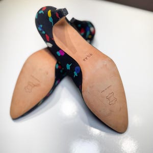 Puede incluir: Un par de tacones negros con un estampado floral multicolor. Los zapatos tienen punta afilada y tac&oacute;n peque&ntilde;o. Las suelas son de color marr&oacute;n claro y est&aacute;n marcadas con "9 1/2 AA" y "MADE IN ITALY".